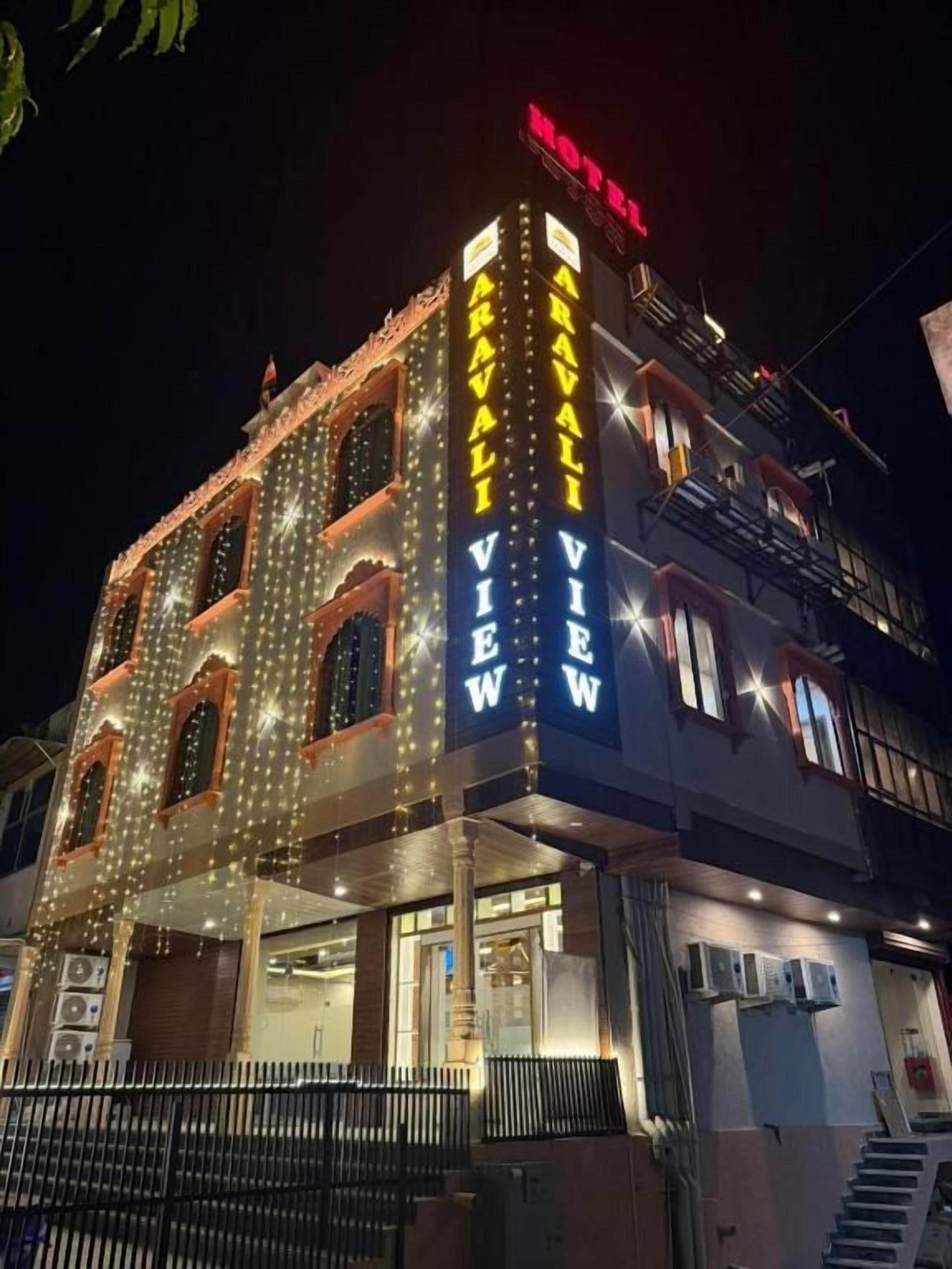 Un hôtel avec une enseigne lumineuse, de nombreuses fenêtres et un escalier menant à l’entrée.