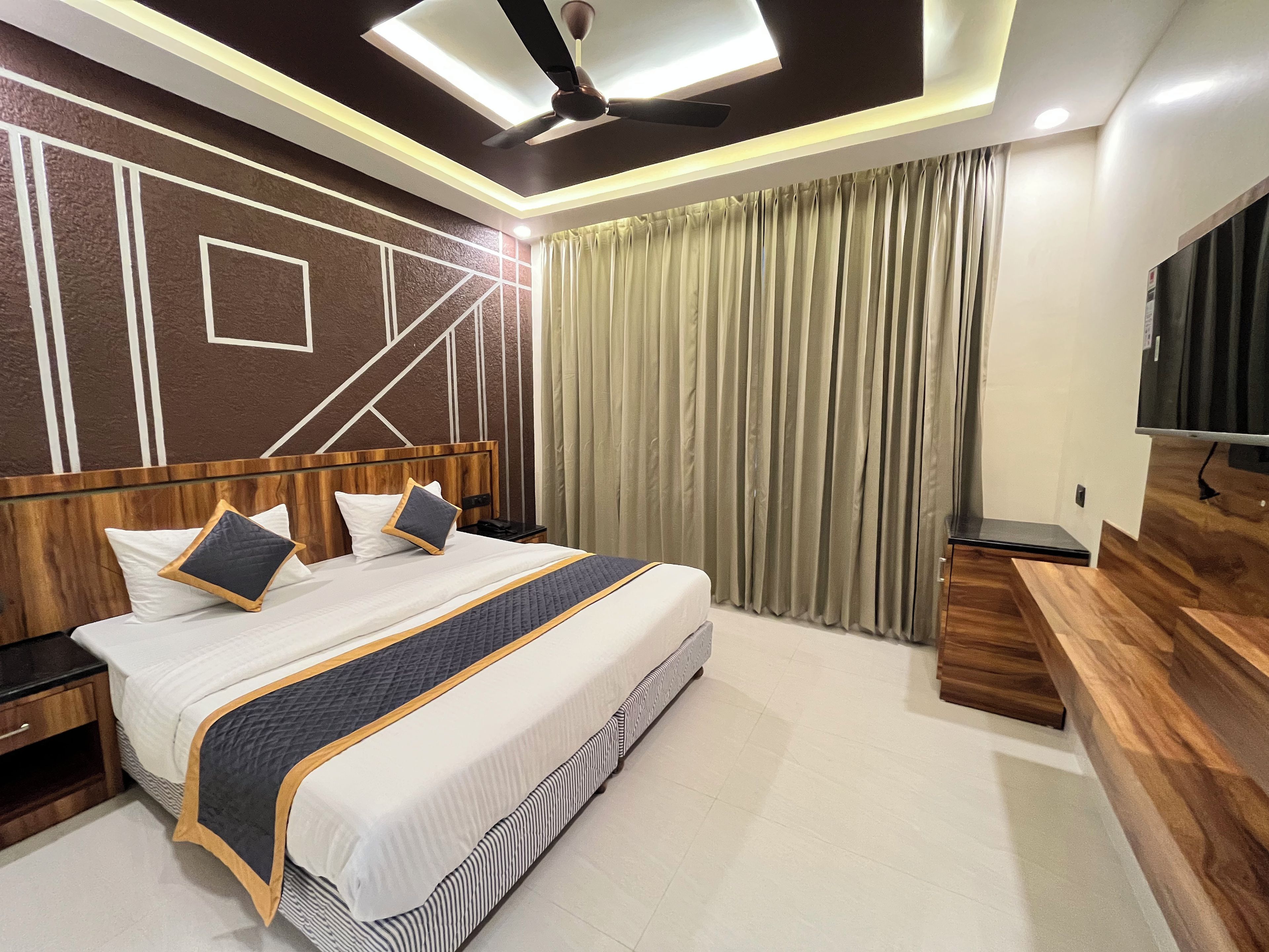 Une chambre d’hôtel moderne dotée d’un grand lit, d’une tête de lit en bois, d’un téléviseur à écran plat et d’un ventilateur de plafond.