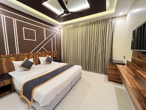 Een moderne hotelkamer met een groot bed, een houten hoofdbord, een flatscreen televisie en een plafondventilator.