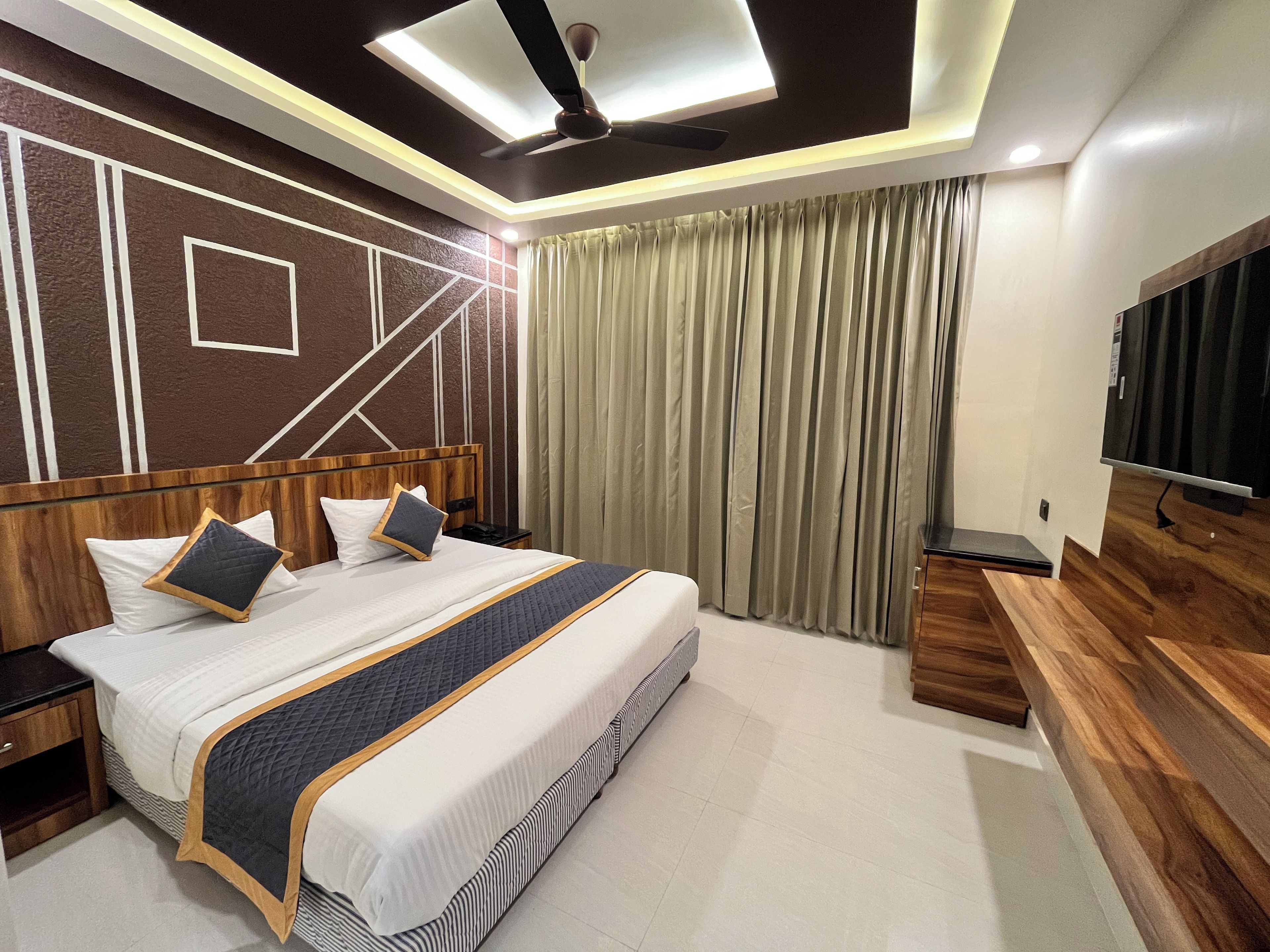 A modern hotel room with a large bed, a ceiling fan, a television, and a wooden side table.