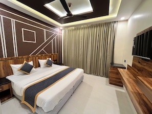 Een moderne hotelkamer met een groot bed, een plafondventilator, een televisie en een houten nachtkastje.