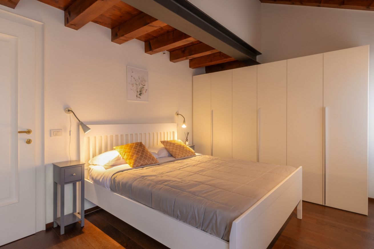 A bedroom with a bed, bedside tables, a wardrobe, and a ceiling with exposed beams.