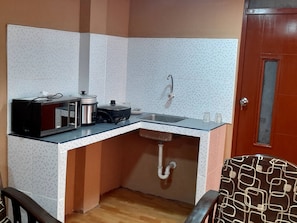 A compact kitchen with a sink, a stove, and a microwave. - Alojamiento Kely (Callao)
