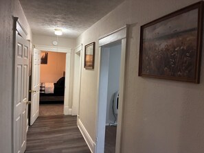 A hallway with a carpeted floor, white walls, and a ceiling light. There are doors on both sides, one leading to a room with a bed and a picture on the wall. - Serene 2-bedroom house with AC in charming Charleston location near all amenitie (Charleston)