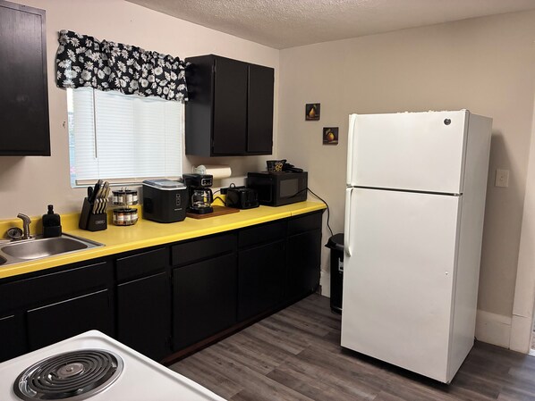 A kitchen with a yellow countertop, black cabinets, a white refrigerator, and a window with blinds.