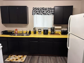 Cocina con armarios negros, encimera amarilla, cafetera y refrigerador.