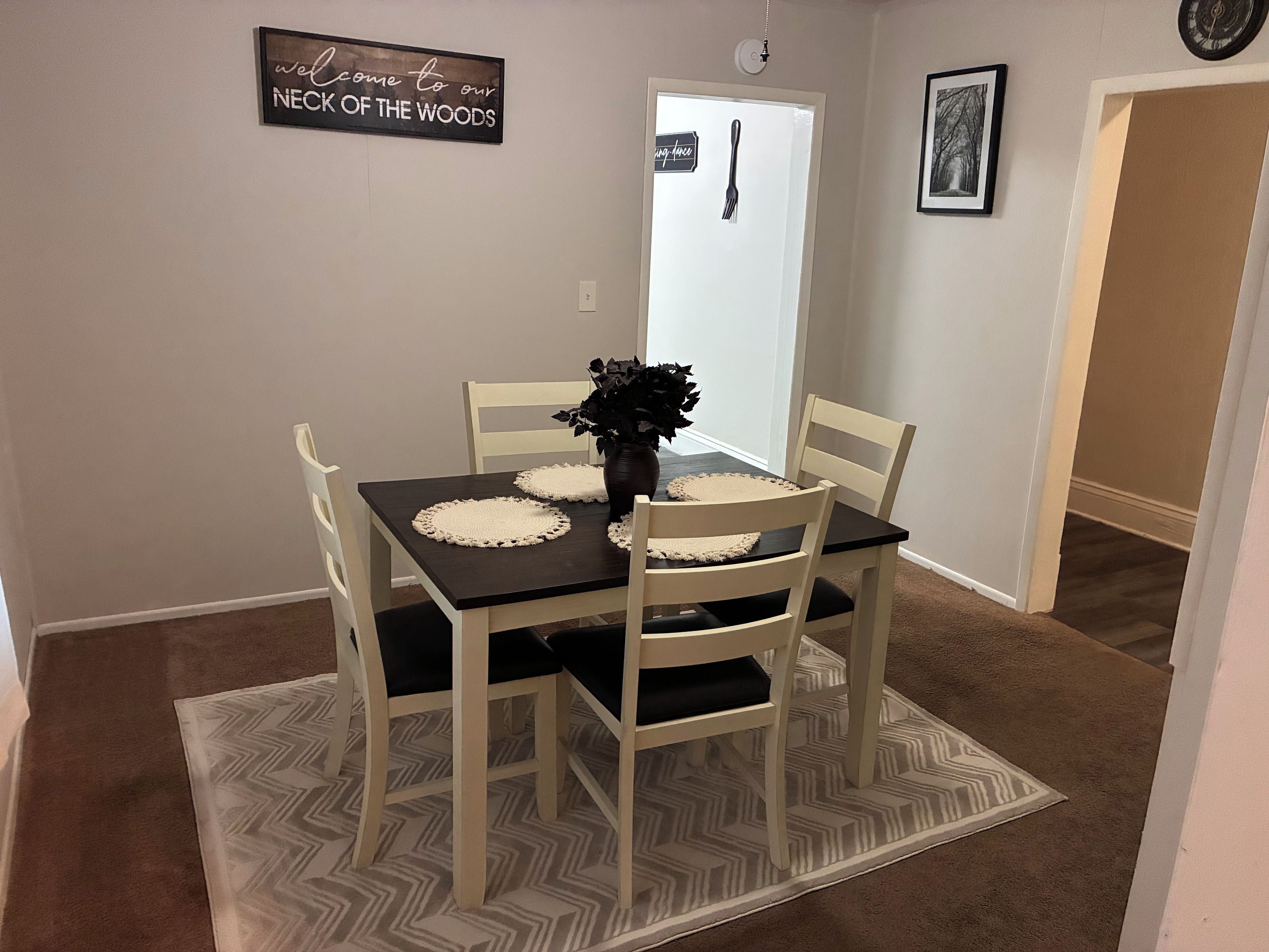 Ruokailutila, jossa on neljälle katettu pöytä, jonka ympärillä on tuoleja, koristeellinen kasvi ja tervetulotoivotus.