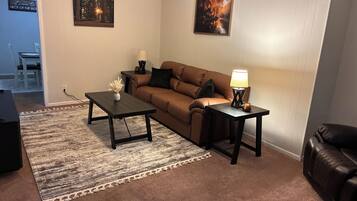 A living room with a brown sofa, a coffee table, a side table with a lamp, and two framed pictures on the wall.