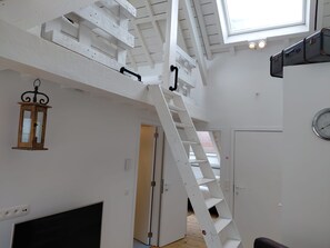 Un intérieur blanc avec un plancher en bois, une cheminée noire, un escalier blanc et une lucarne.