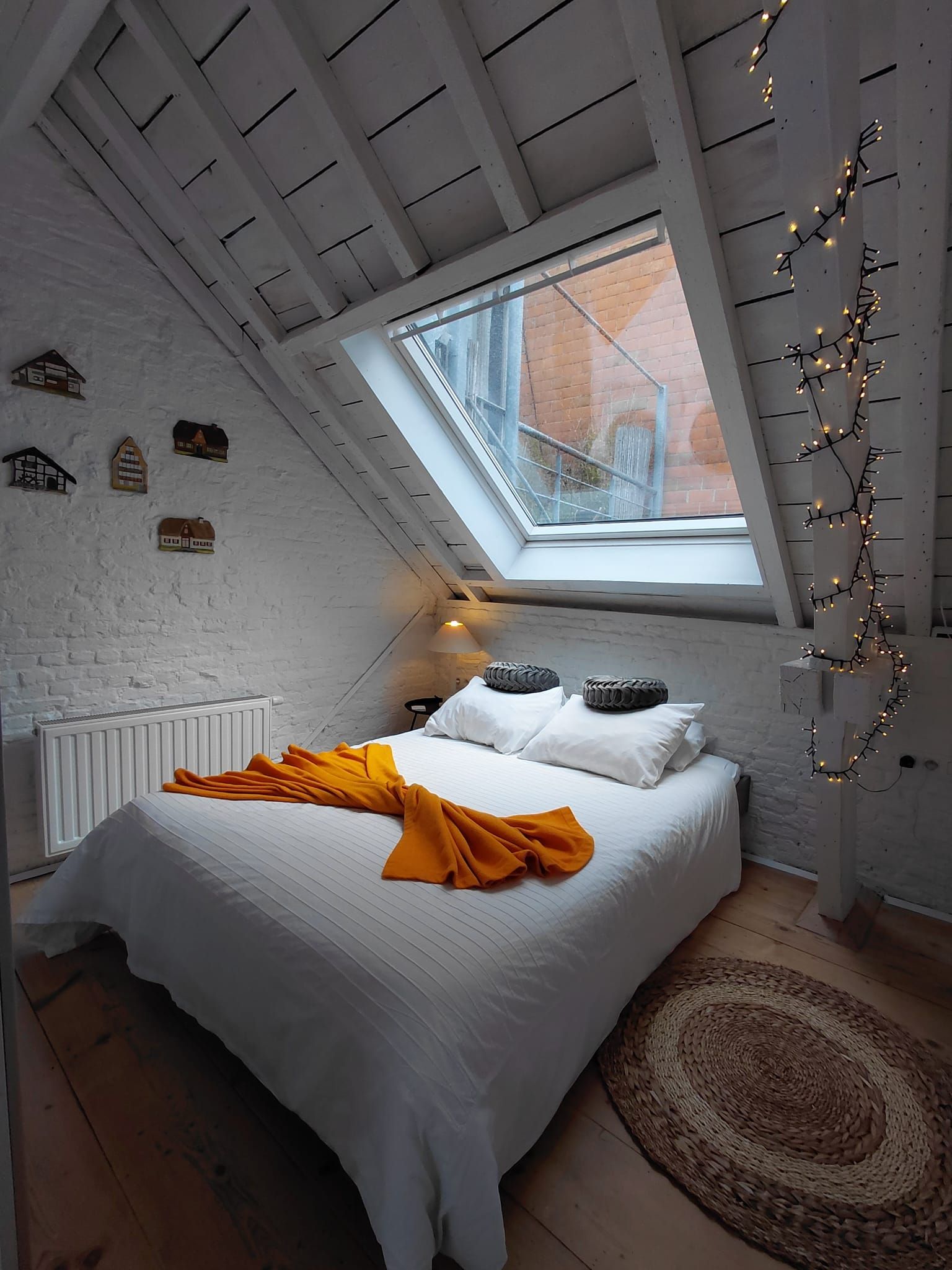 A bedroom with a sloped ceiling, a skylight, a bed with white bedding and a yellow throw, and a radiator.