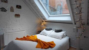 A bedroom with a sloped ceiling, a skylight, a bed with white bedding and a yellow throw, and a radiator.