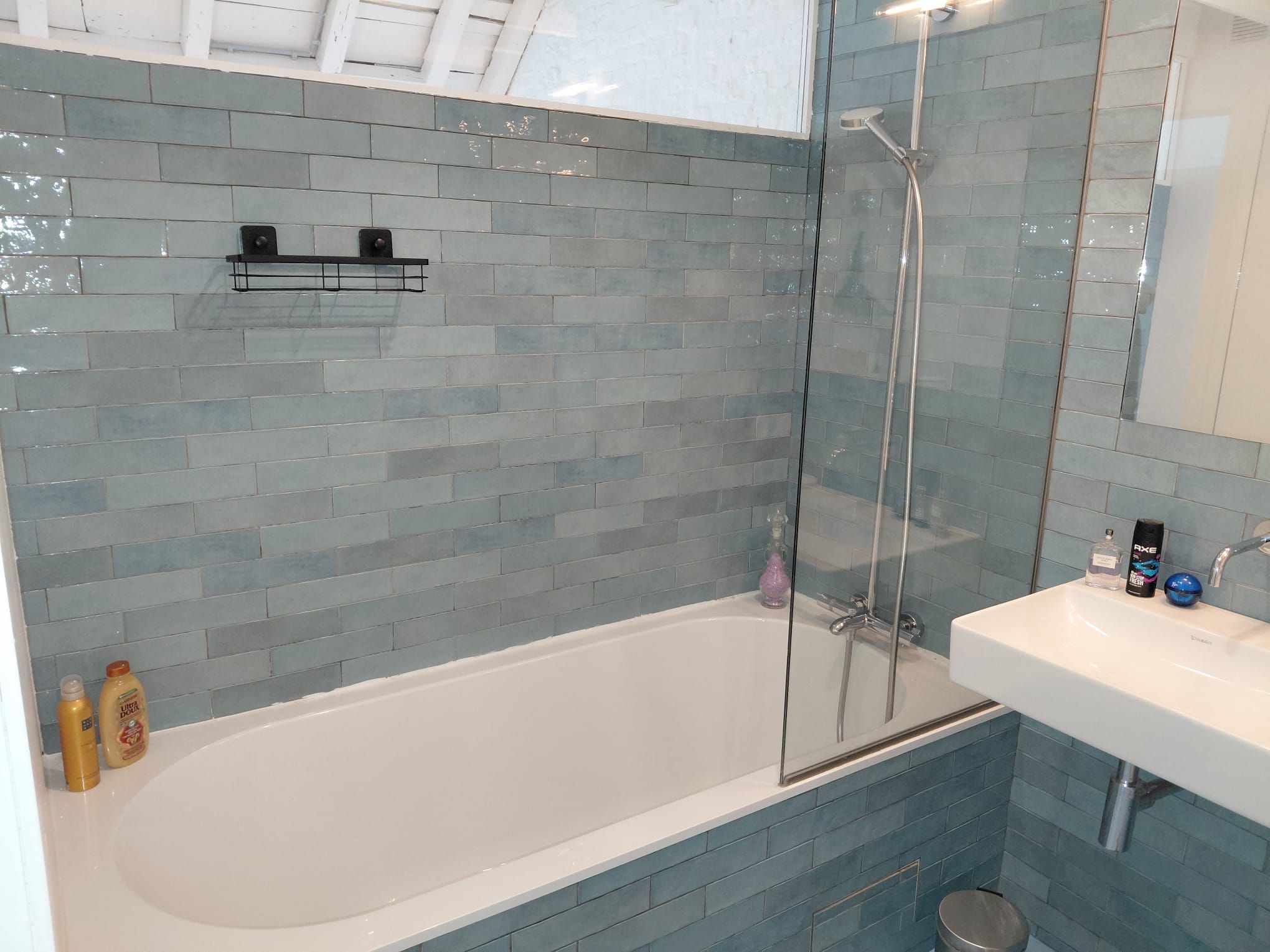 Une salle de bain avec une douche à parois de verre, une baignoire blanche et un lavabo équipé de produits de toilette.