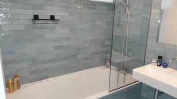 Une salle de bain avec une douche à parois de verre, une baignoire blanche et un lavabo équipé de produits de toilette.