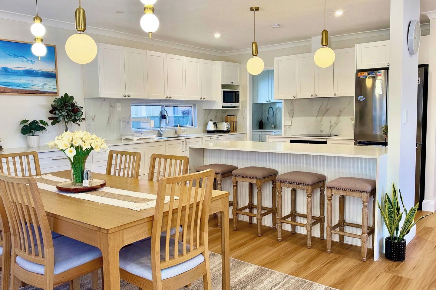 Une cuisine moderne avec des meubles blancs, un îlot central, des tabourets de bar et des luminaires suspendus.