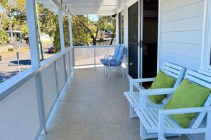 A covered porch with white railings, two white benches with green cushions, and a blue chair. - Holiday House Southport, GOLD COAST (Southport)