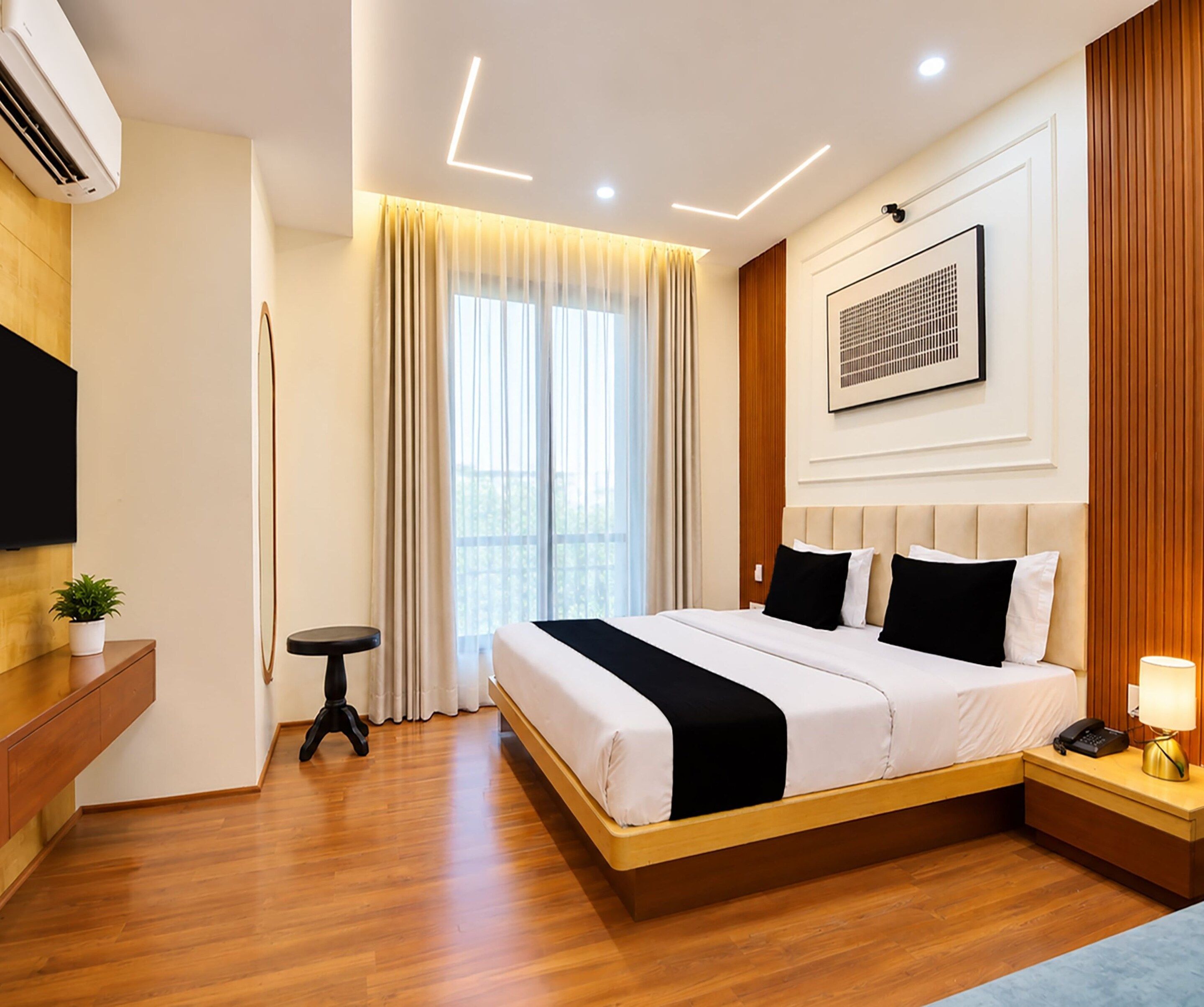 A modern hotel room with a large bed, a bedside table with a lamp, a mounted TV, and a window with curtains.