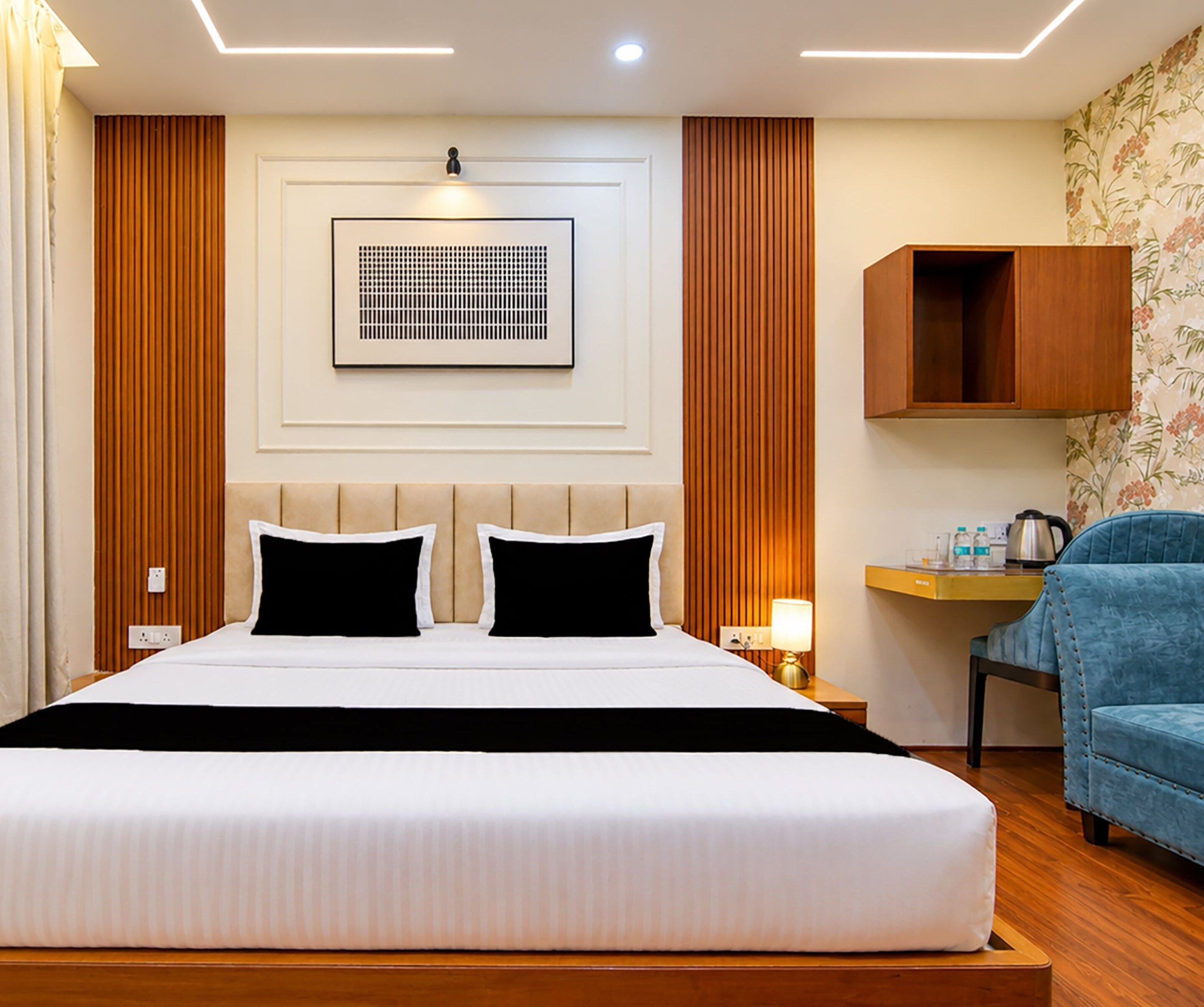A hotel room with a large bed, a bedside table with a lamp, a wooden headboard, and a blue armchair.