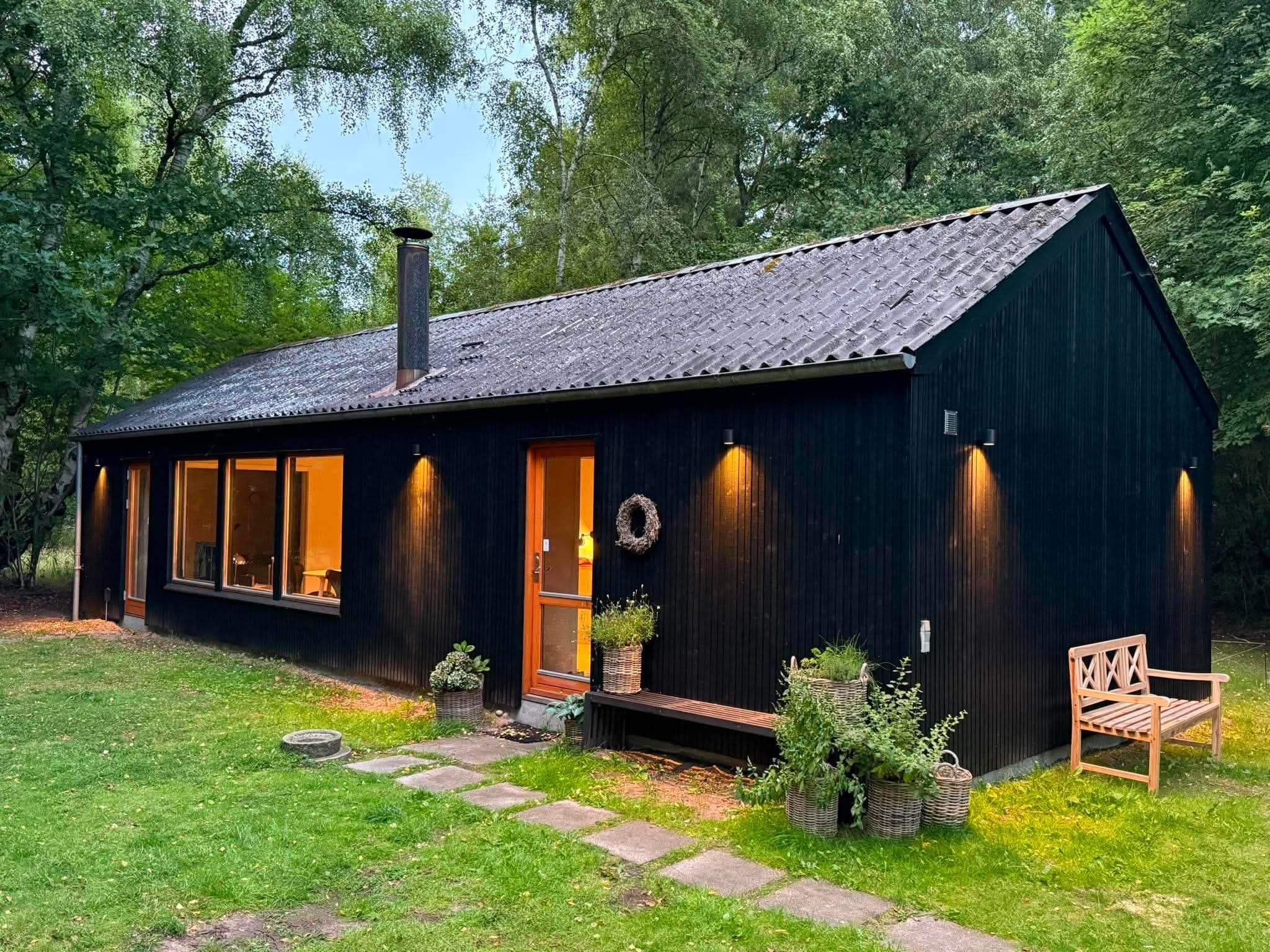 Une cabane en bois sombre, dotée d’un toit en pente, de grandes fenêtres et d’une cheminée.