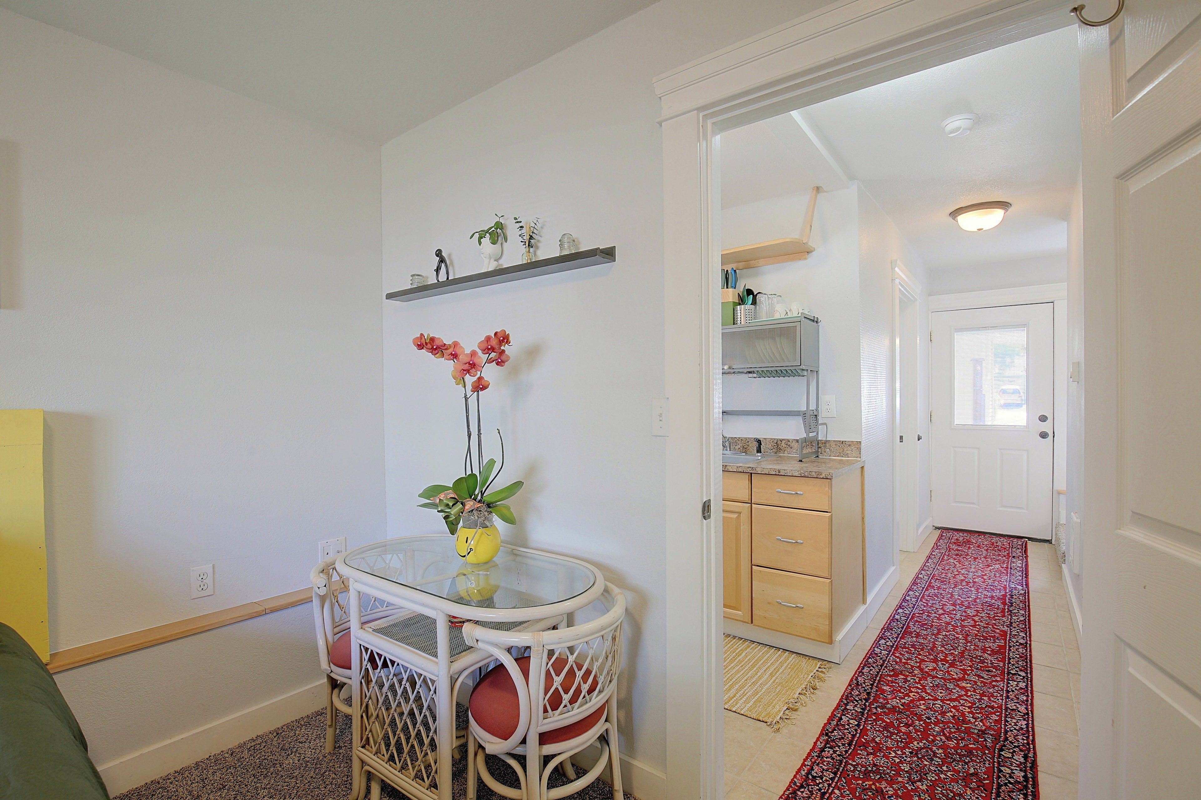 Un espacio habitable compacto con zona de comedor que incluye una mesa redonda y sillas, una cocina con armarios de madera y un pasillo con un tapete estampado.