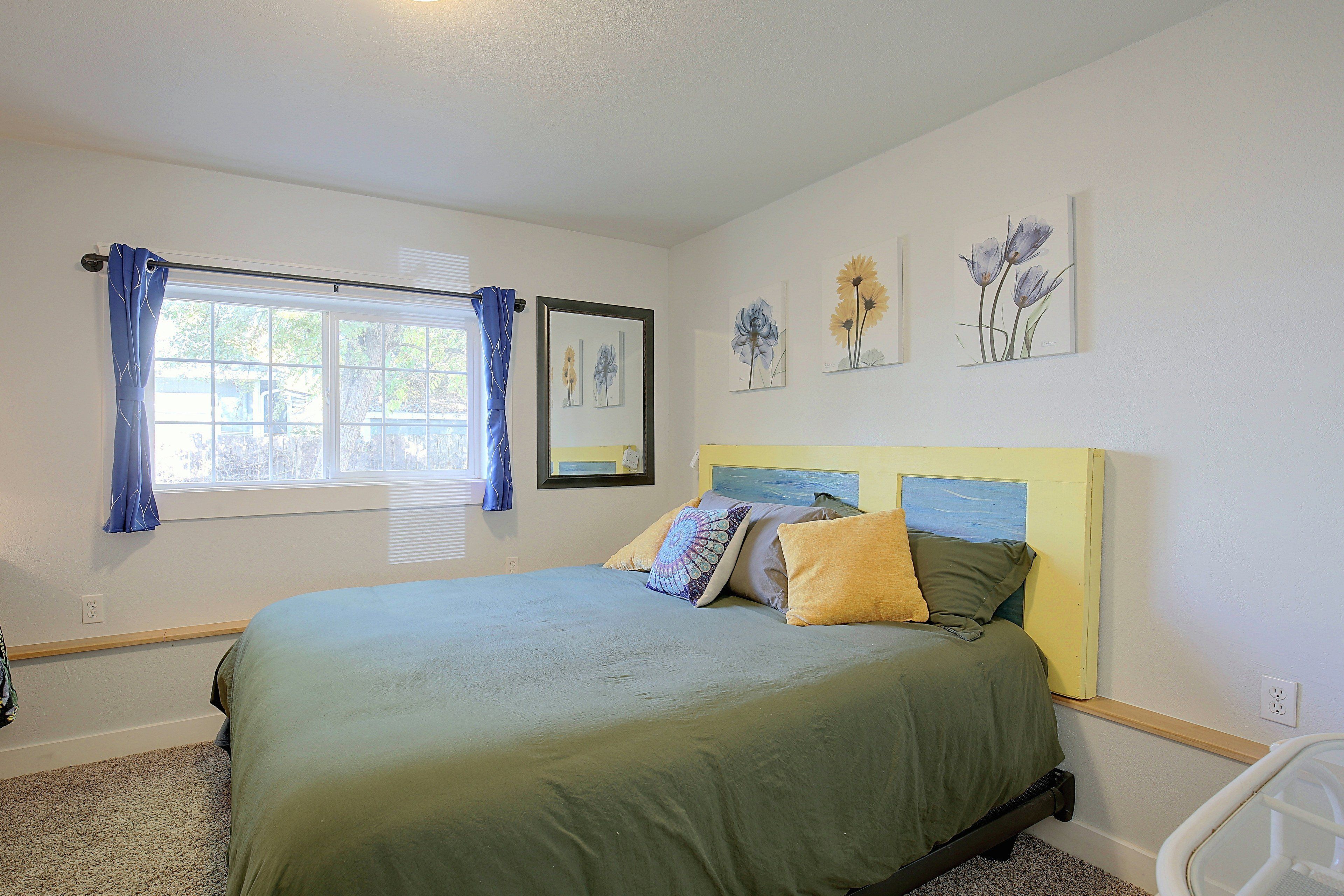 A bedroom with a bed, a window with curtains, and wall-mounted artwork.