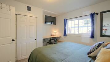 Un dormitorio con cama, ventana con cortinas, televisor de pantalla plana y una puerta.