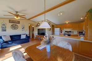 A spacious living area with a wooden dining table, a blue sofa, and a ceiling fan. - Montana Mountain Escape! Views, Trails & Toys (Dupuyer)