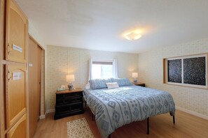 Une chambre à coucher comprenant un lit, deux tables de chevet, une commode, une coiffeuse, une fenêtre avec des rideaux et un mur orné d’un miroir décoratif.