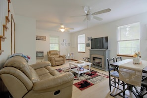 A living room with a fireplace, a television, a ceiling fan, and a large window with blinds. - Wooded Dunlap Retreat w/ Creek & Fire Pit (Graysville)