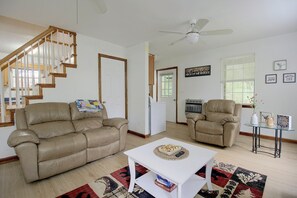 A living room with two beige leather sofas, a white coffee table, a red and black patterned rug, a ceiling fan, and a staircase with wooden railings. - Wooded Dunlap Retreat w/ Creek & Fire Pit (Graysville)