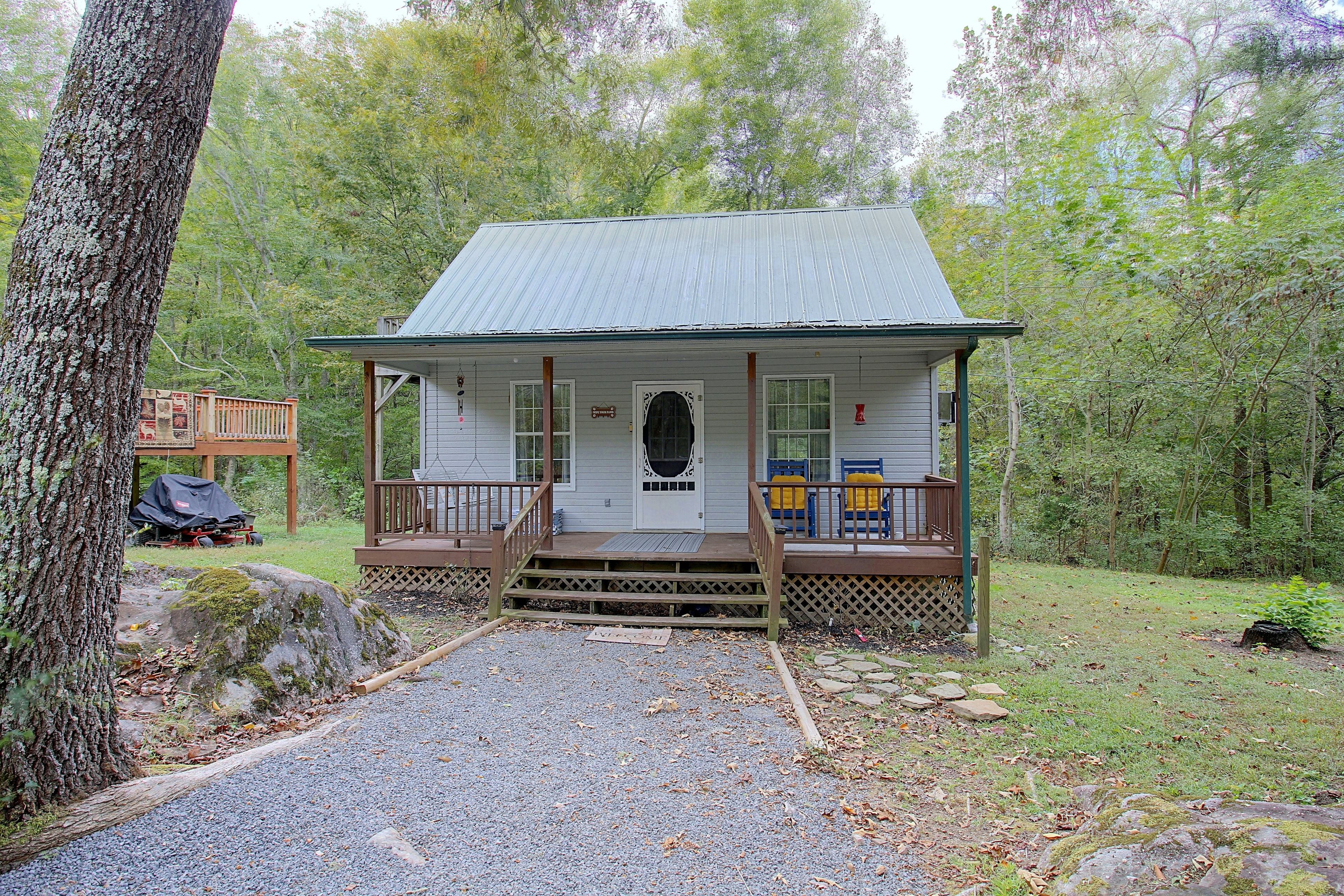 A small cabin with a porch, a covered deck, and a gravel driveway.