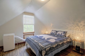 Un dormitorio con techo inclinado, una cama con ropa de cama estampada, un calentador, una ventana con persianas y una pared con textura.