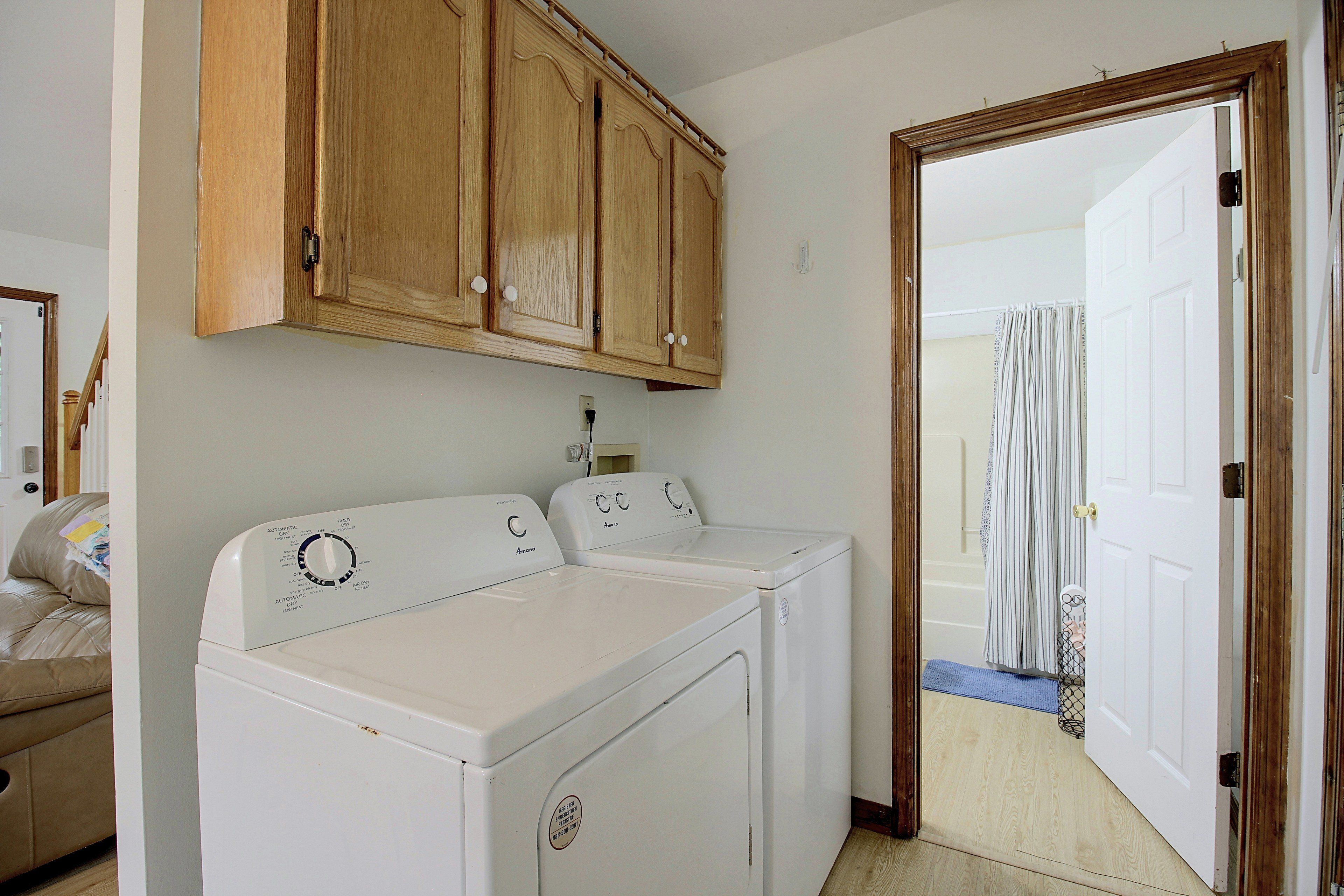 A laundry room with two white front-loading washing machines, wooden cabinets above, and a door leading to another room.