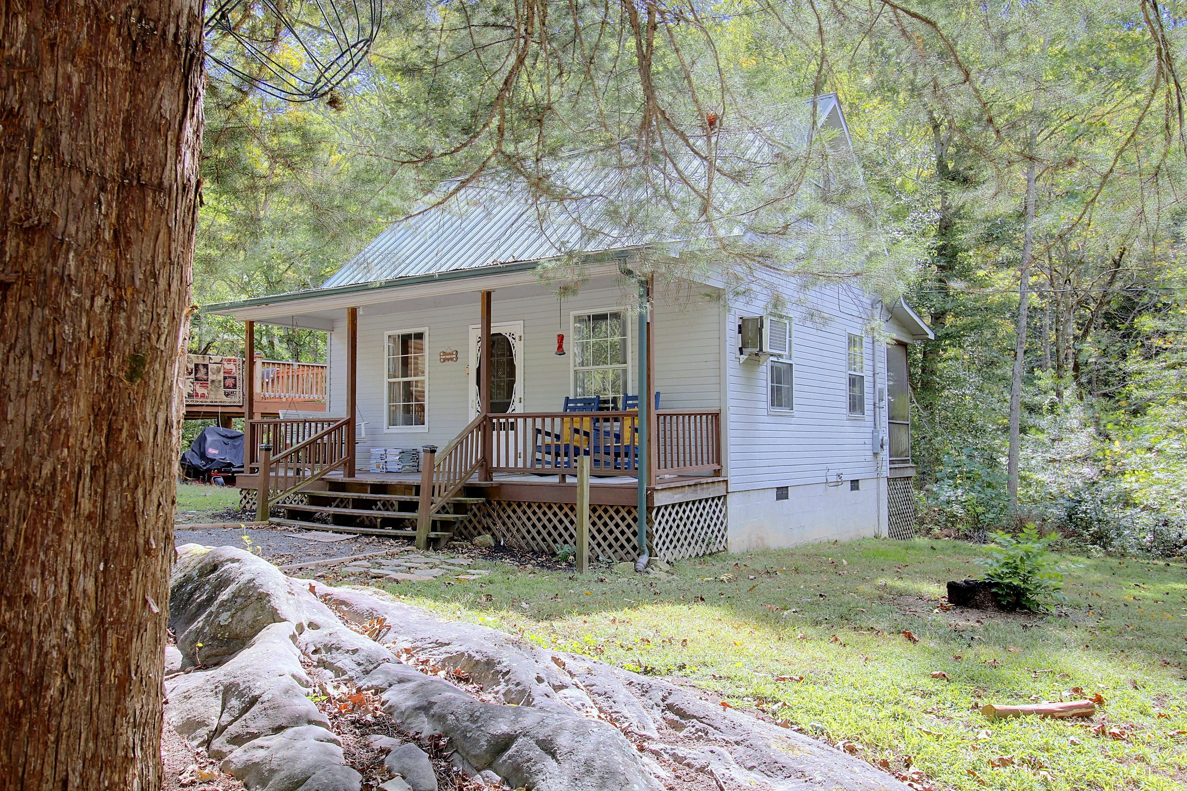 A small cabin with a porch, surrounded by trees and a grassy area.