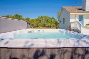 A hot tub with a wooden deck, a white house with a blue door, and a clear blue sky.