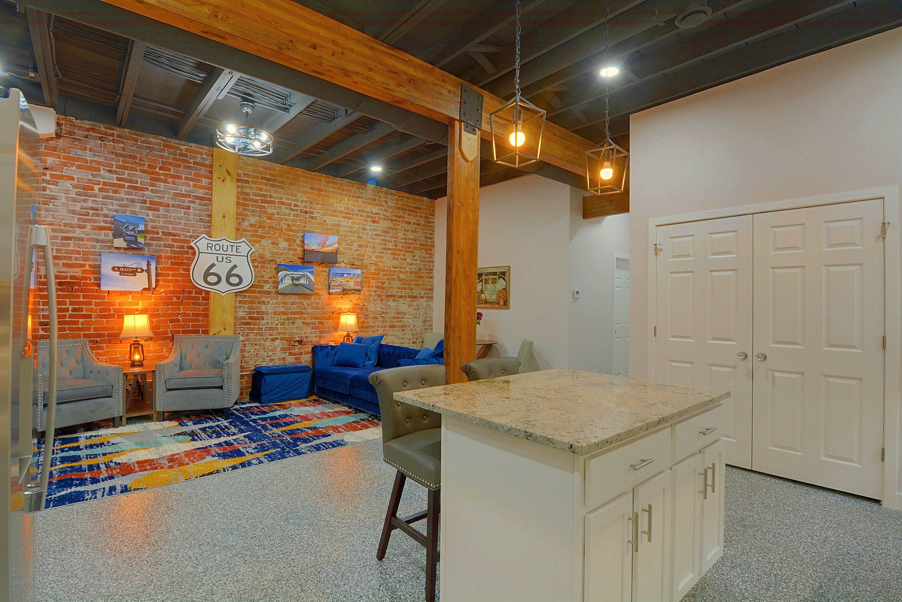 A room with a brick wall, a sofa, a coffee table, and a kitchen area with a countertop and cabinets.