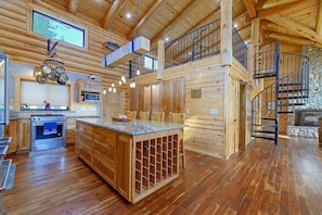 A spacious log cabin with a kitchen featuring a built-in oven, a dining area with wooden chairs, and a stone fireplace.