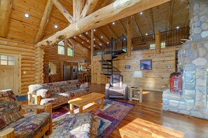 A log cabin interior with a wooden floor, a sofa, a recliner, a fireplace, and a stone wall.