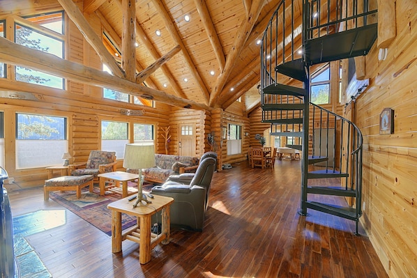 A log cabin interior with a wooden floor, a fireplace, a sofa, and a staircase.