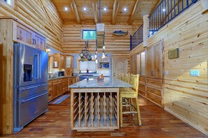A log cabin interior with a central island, wooden cabinets, and a stainless steel refrigerator.