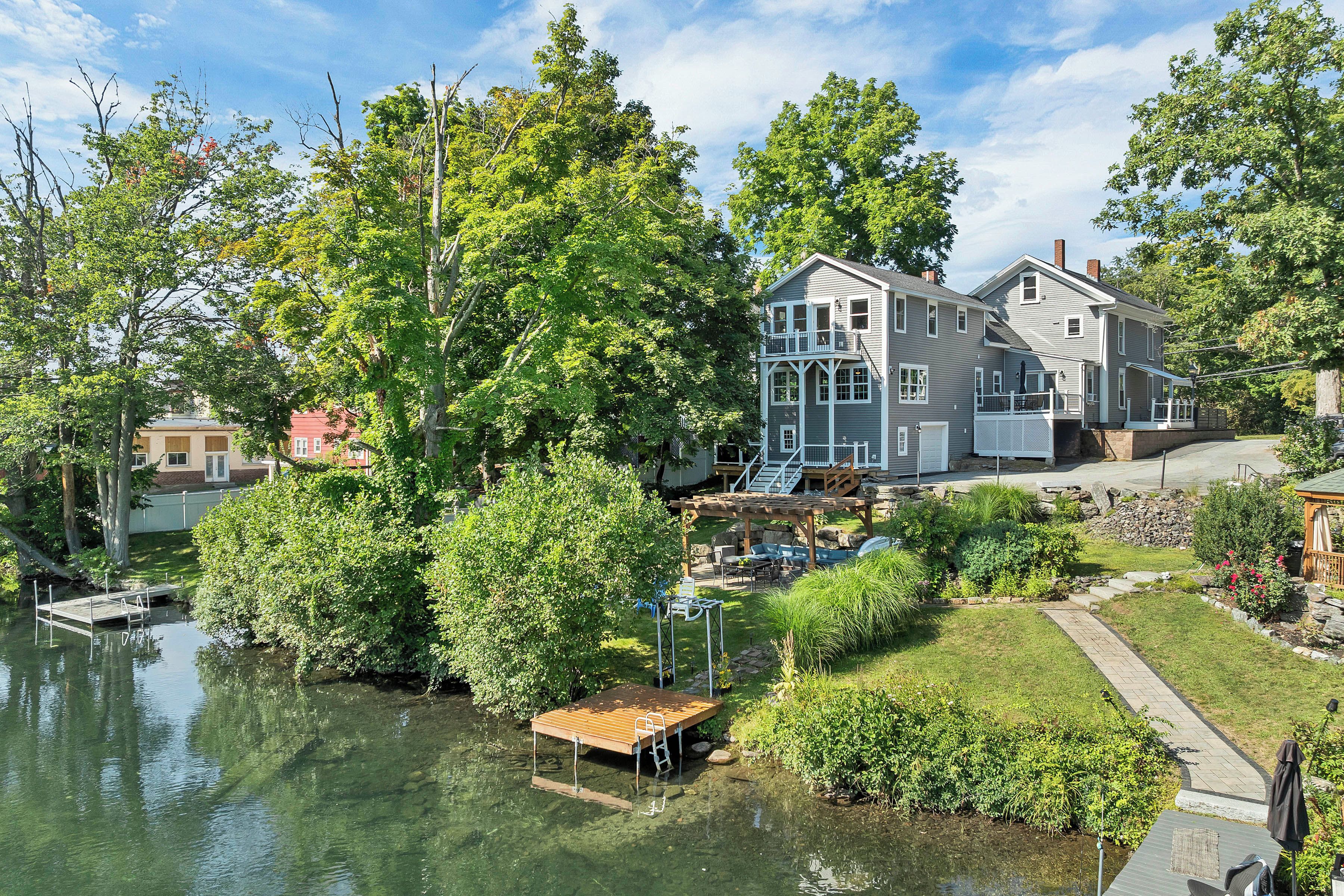 A residential property with a dock extending into a body of water, surrounded by lush greenery and a well-maintained lawn.