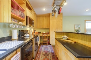 A kitchen with wooden cabinets, a microwave, a stove, and a dining area with a chair and table.
