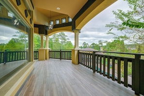 A covered outdoor balcony with a wooden floor, railings, and a view of trees.