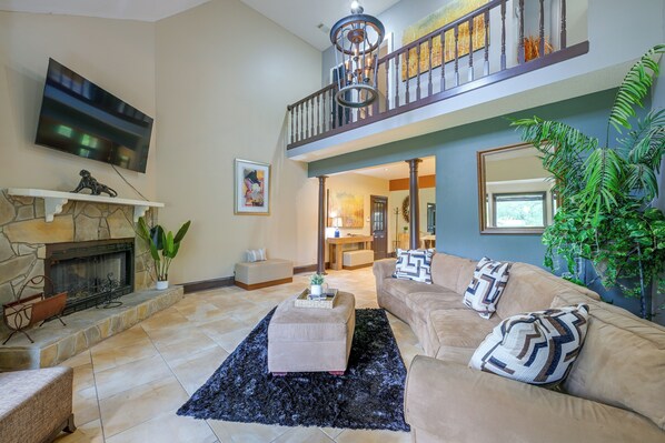 A spacious living room with a fireplace, a large sofa, a coffee table, and a staircase leading to an upper level.