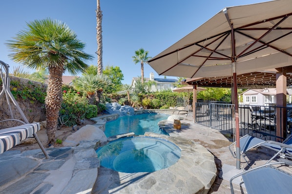 A pool area with a hot tub, lounge chairs, and a pergola with a canopy.