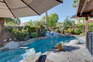 A swimming pool with clear blue water, surrounded by rocks and plants.
