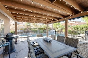 An outdoor patio with a pool, seating, and a pergola with string lights.
