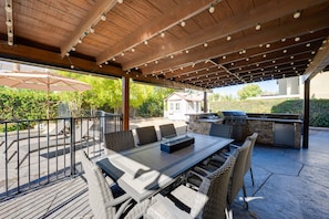 An outdoor patio with a covered seating area, a grill, and a table with chairs.