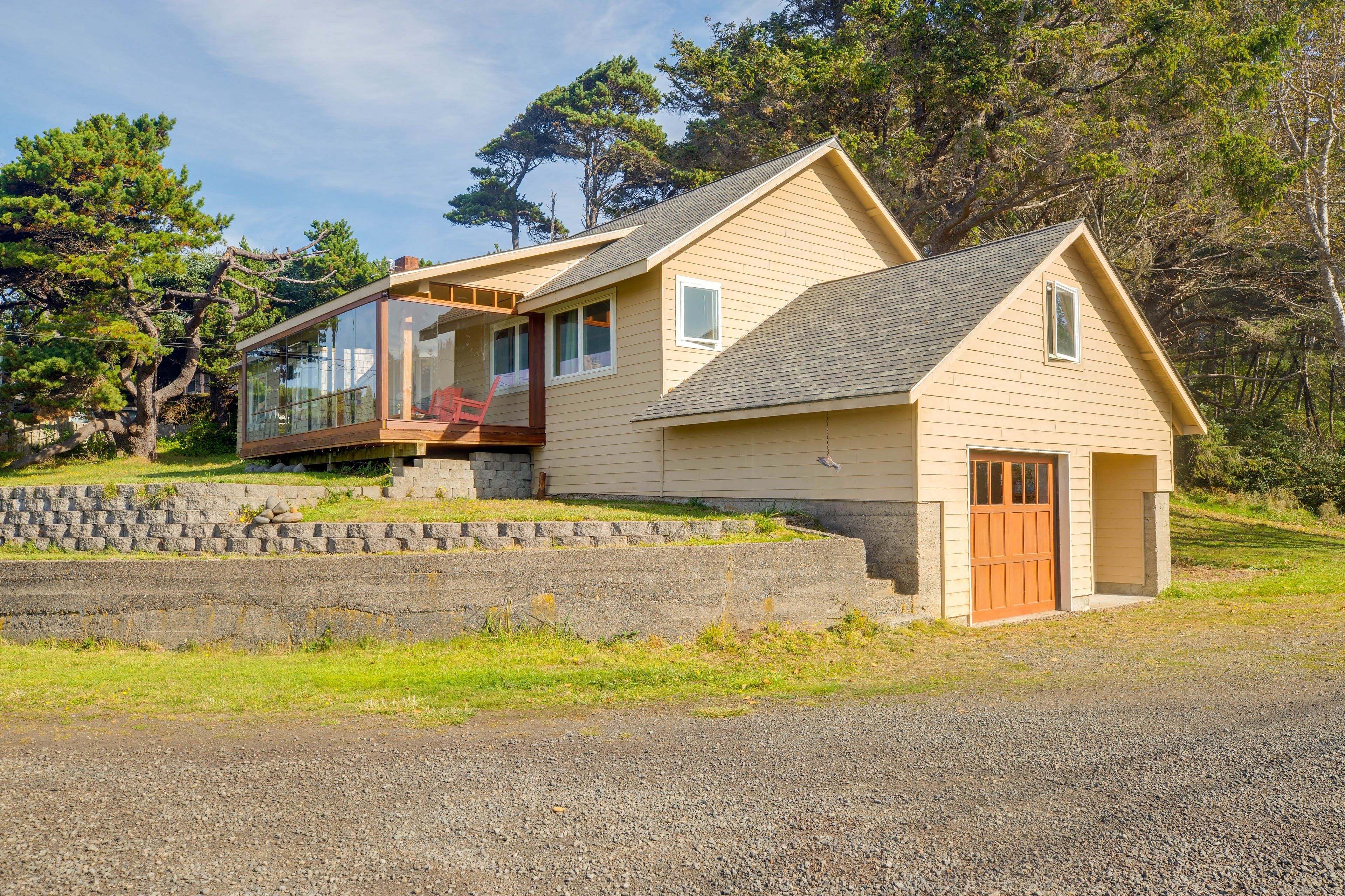 Une maison à deux étages dotée d’une grande baie vitrée, d’une terrasse en bois et d’un mur de soutènement en pierre.
