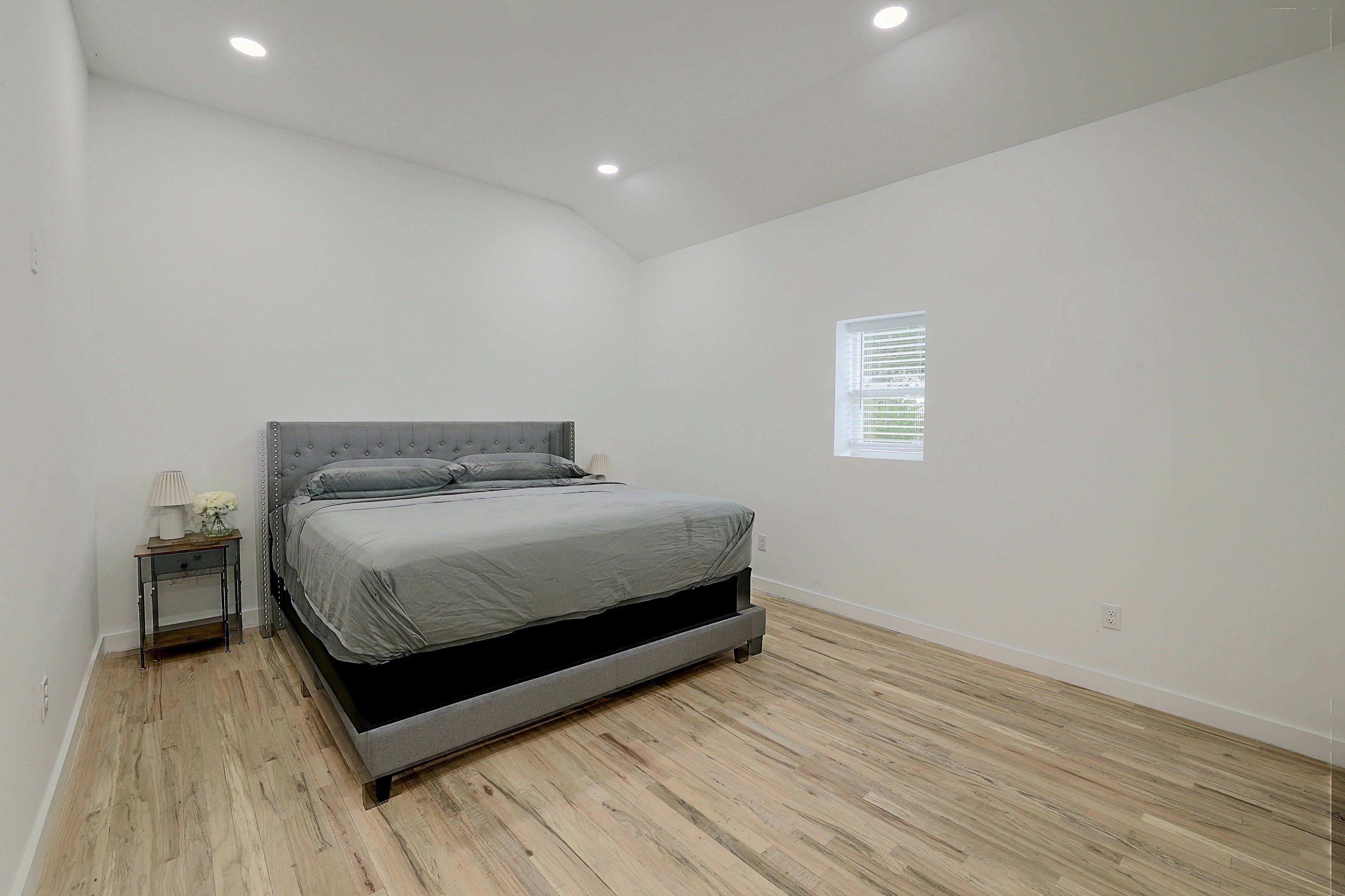 A bedroom with a bed, a nightstand, a lamp, and a window with blinds.