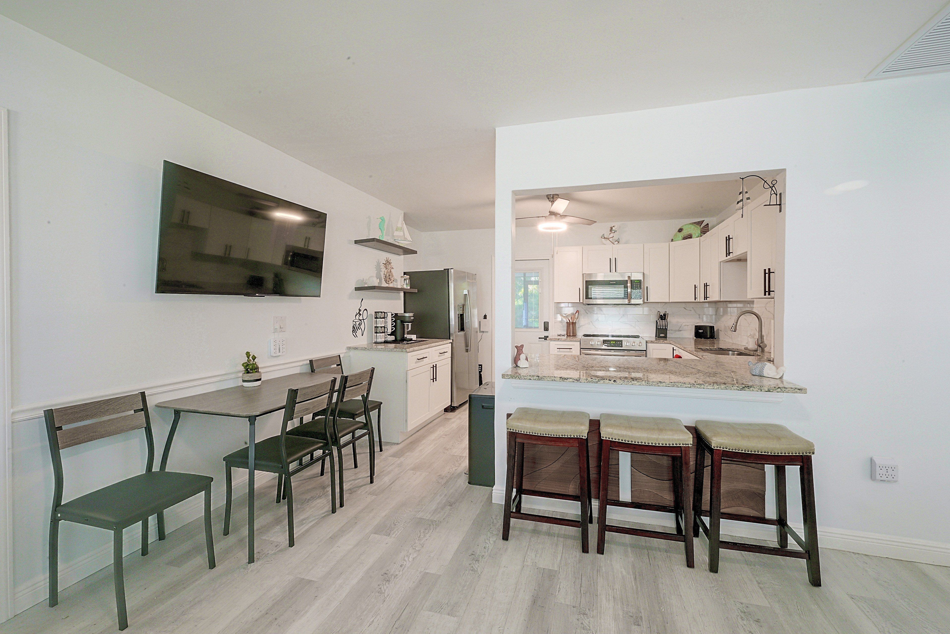 A modern kitchen with a dining area, featuring a flat-screen TV, a refrigerator, and a microwave.